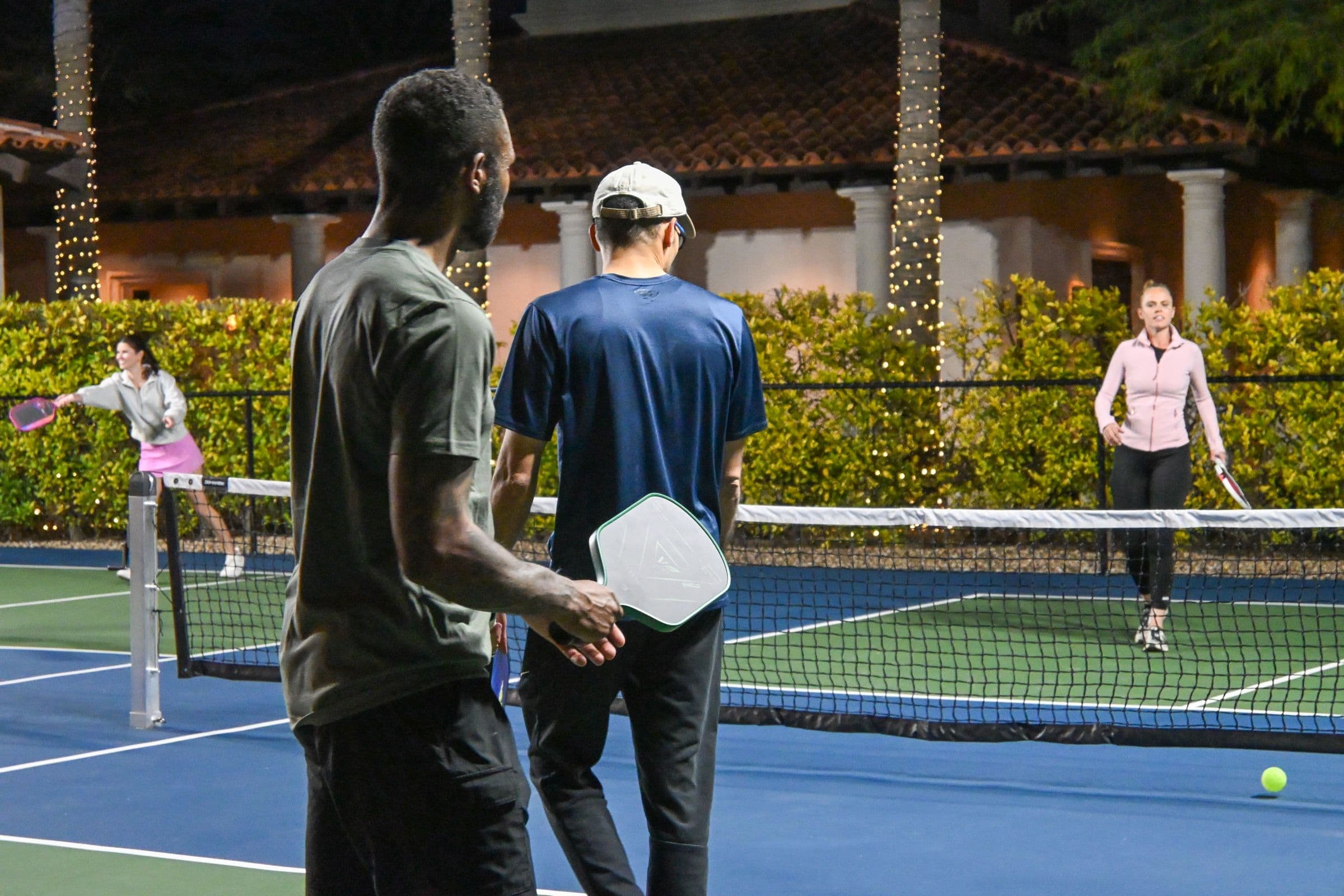 Doubles pickleball match under the lights on a blue court at night
